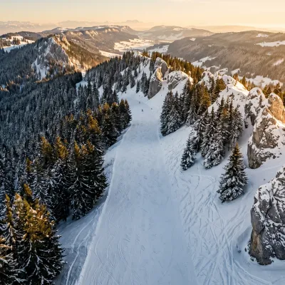 Piste de ski dans le Jura bernois, avec des sapins enneigés et une topographie escarpée sous une lumière de fin de journée.