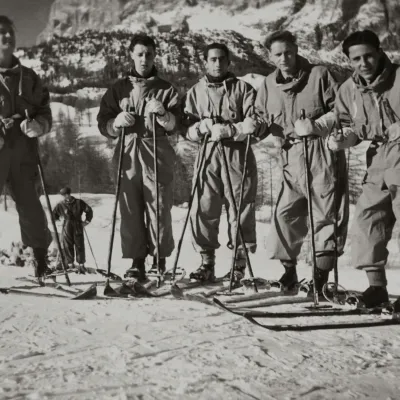 Photographie d'archive en noir et blanc de pionniers du ski alpin en tenue d'époque, posant avec des skis en bois sur une pente enneigée.