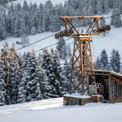 Ancien téléski à perches sur une pente enneigée du Jura bernois, câble et pylône métallique rouillés, lumière rasante d'hiver.